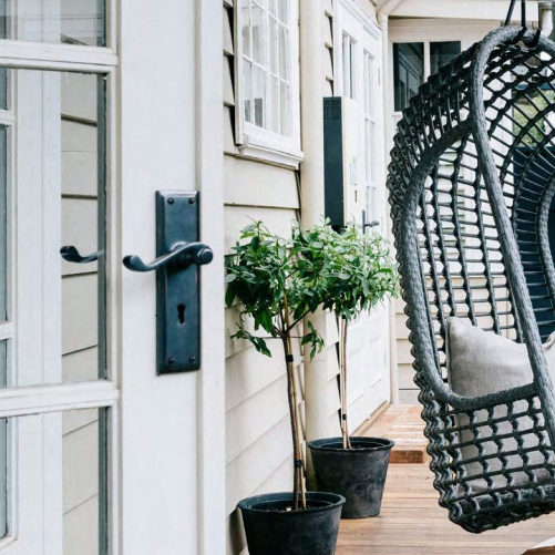 — Port Macquarie Locksmiths In Port Macquarie, NSW A Hanging Chair Is Sitting On A Porch Next To Potted Plants — Port Macquarie Locksmiths In Port Macquarie, NSW