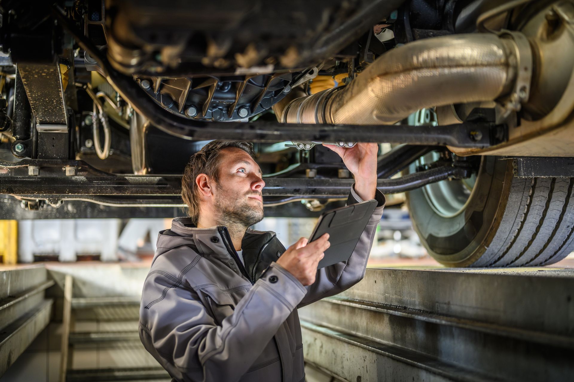 A man is looking underneath a truck while using a tablet.