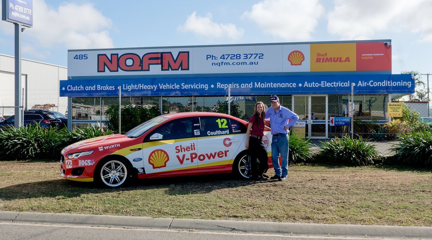 Two men standing next to a red car that says v-power