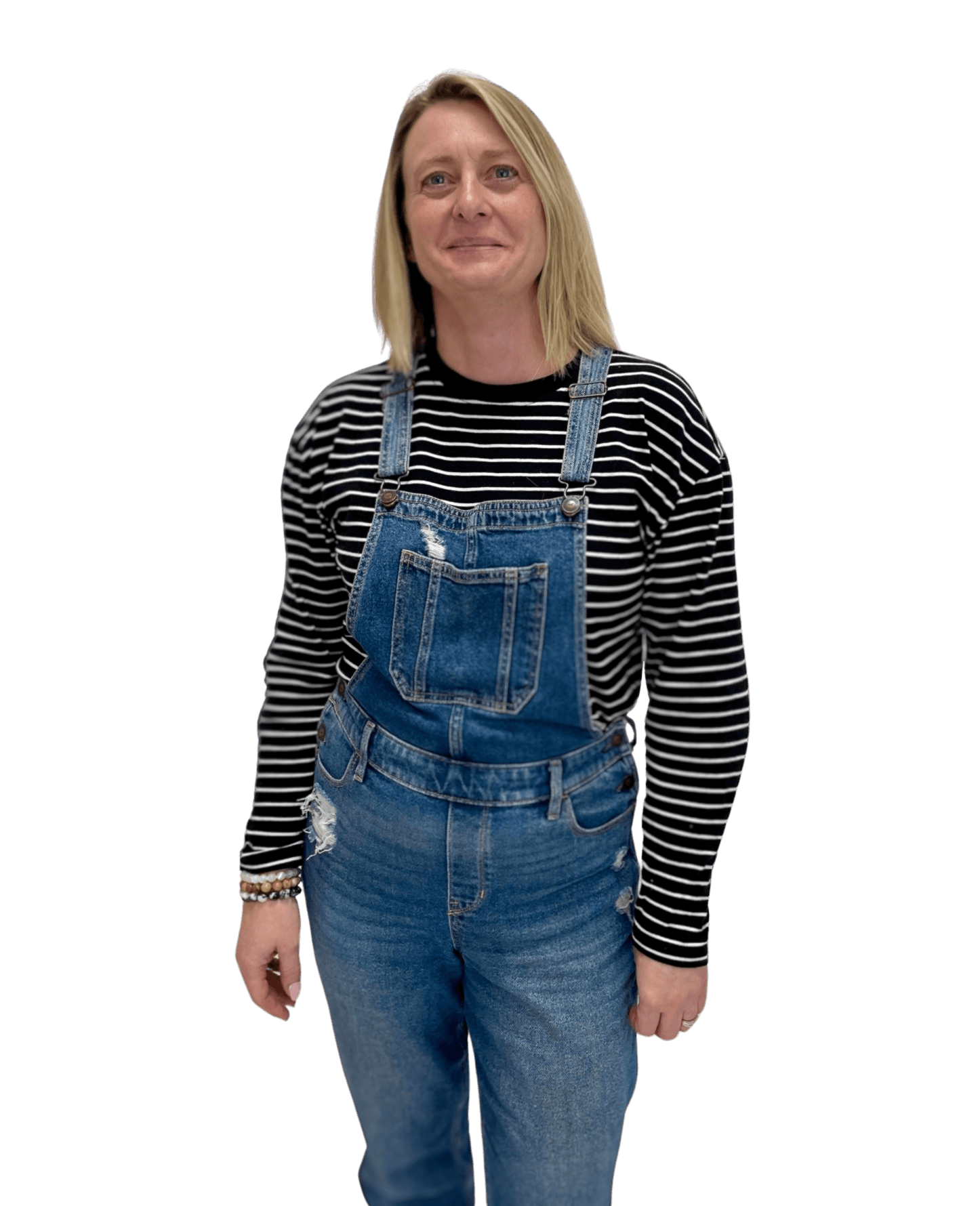 Michelle Winzart wearing overalls and a striped shirt is standing in front of a white background.