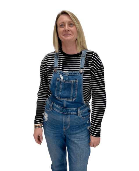Michelle Winzart wearing overalls and a striped shirt is standing in front of a white background.