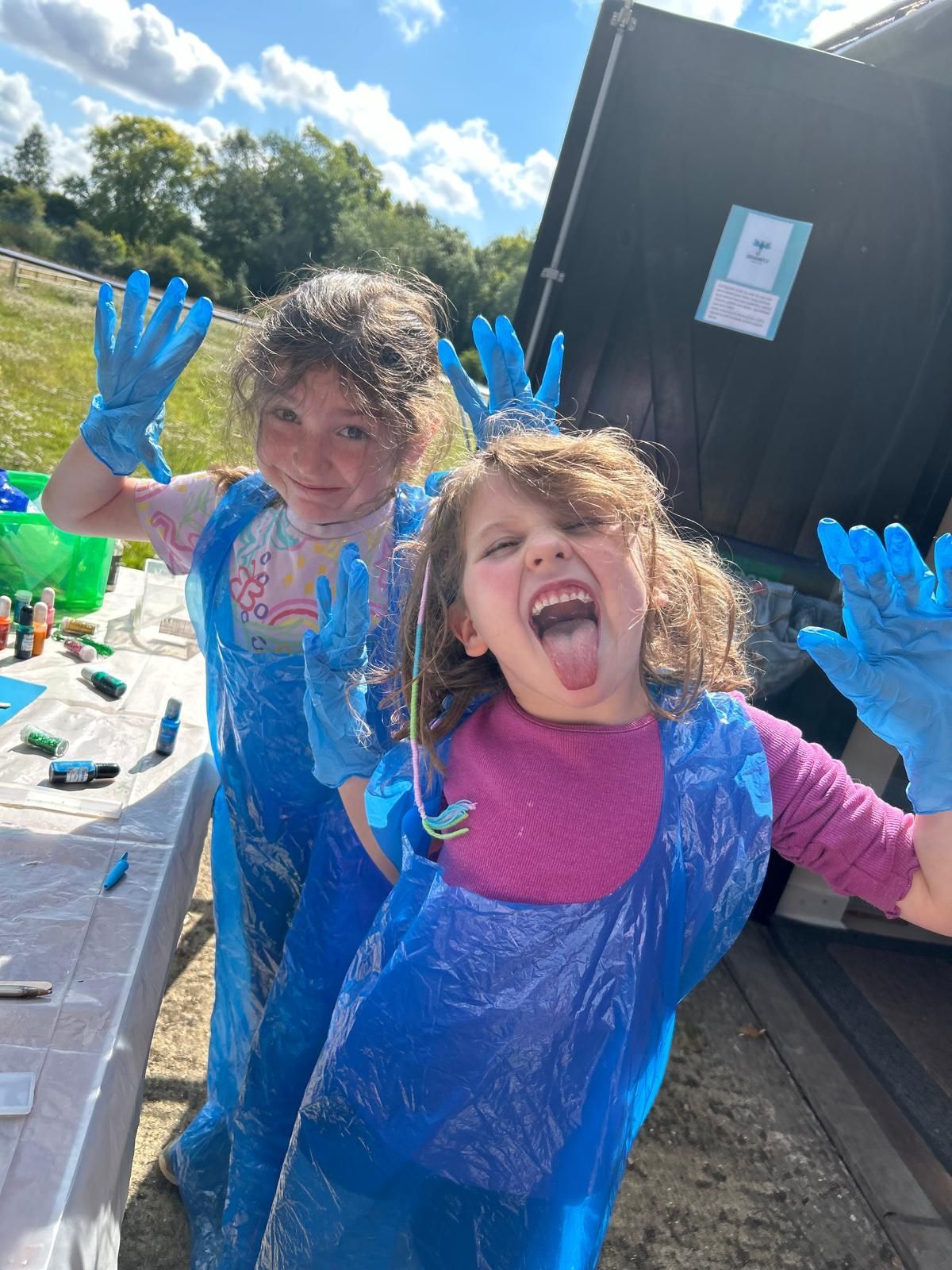 Two little girls wearing blue plastic gloves are standing next to each other  at Dragonfly crafts parties.