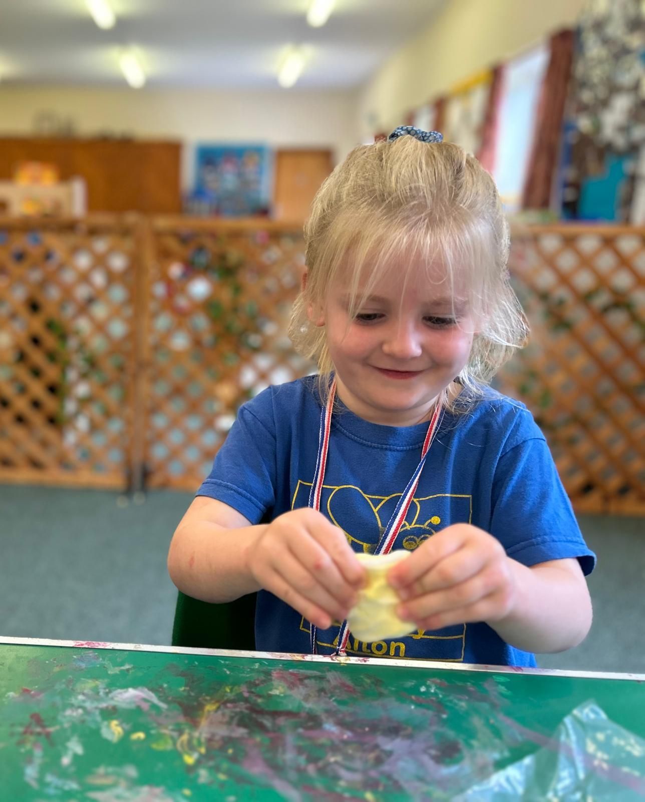 A little girl is sitting at a table playing with clay at Dragonfly craft session.