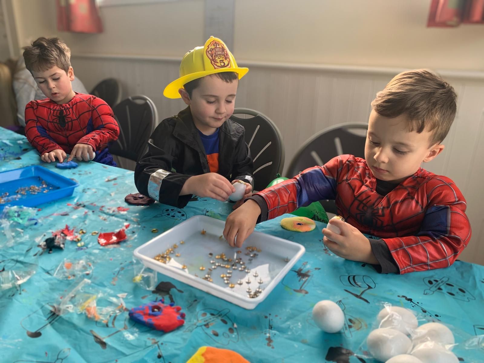 Three young boys in costumes are sitting at a table playing with toys craft party.