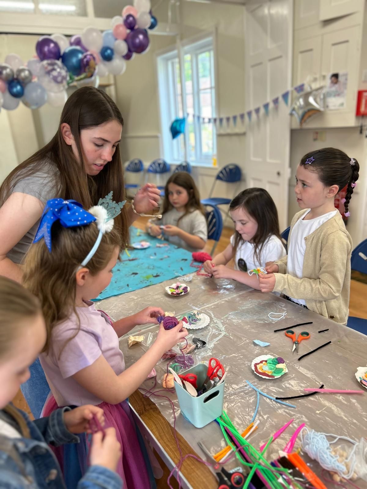 A group of young girls are sitting at a table making crafts for charm party  at Dragonfly crafts parties