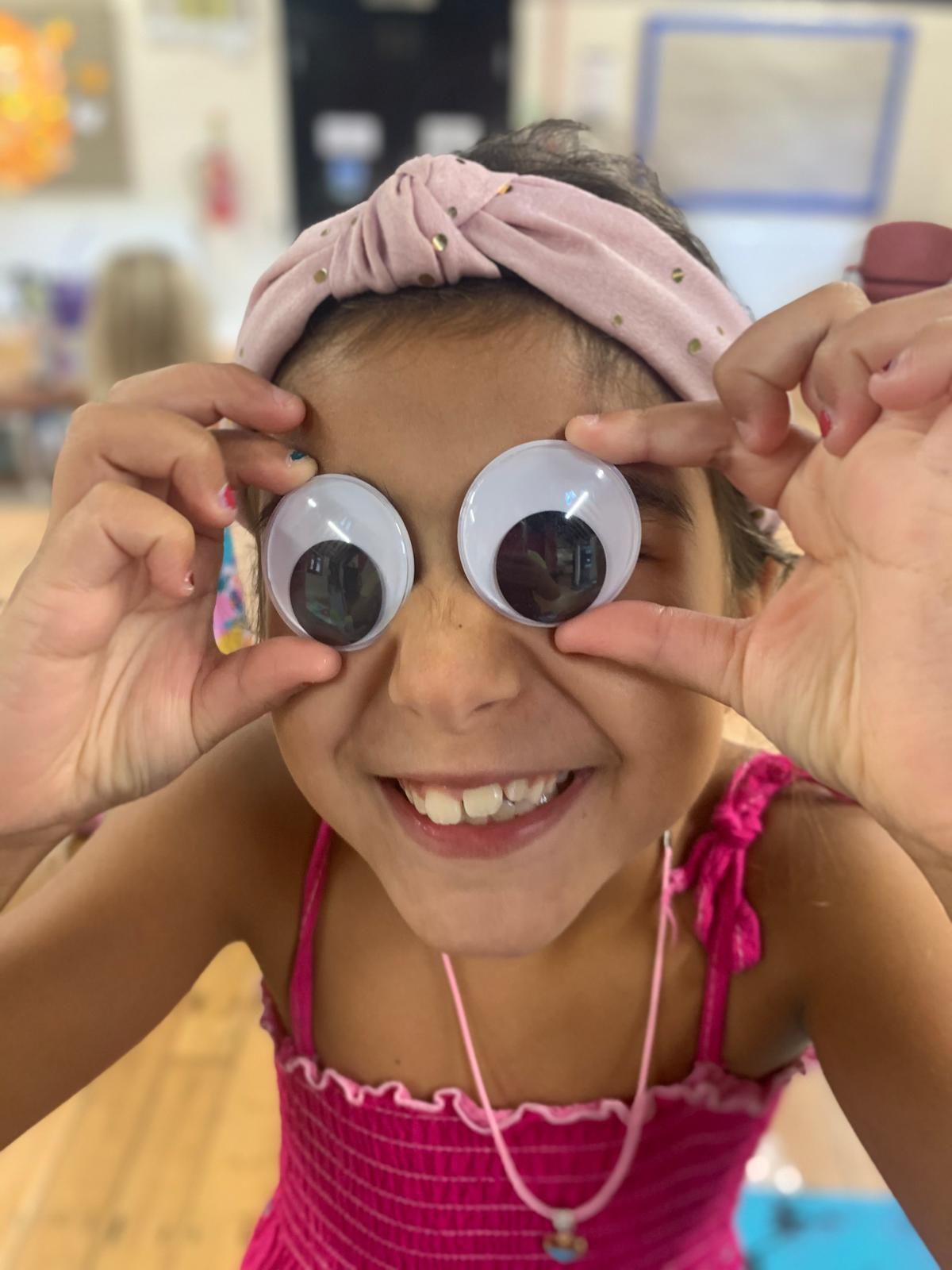 A little girl wearing a pink headband and googly eyes at Dragonfly crafts session