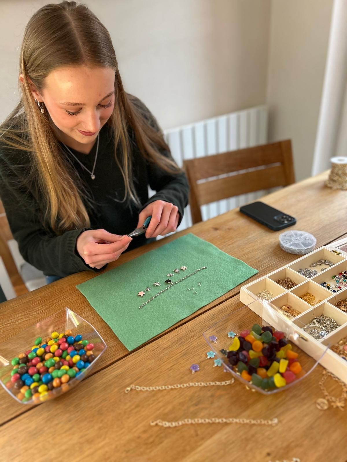 A woman is sitting at a table making a necklace with beads for charm party  at Dragonfly crafts parties