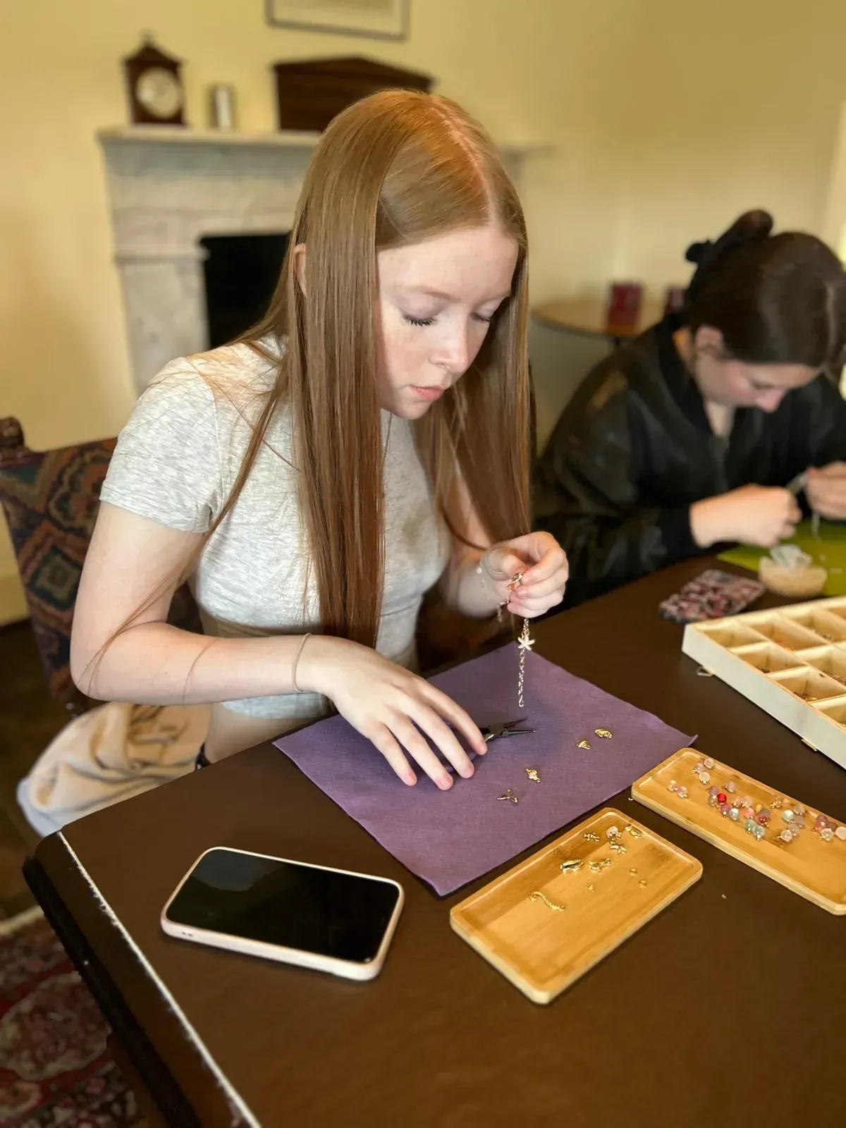 A woman is sitting at a table making a necklace with beads for charm party  at Dragonfly crafts parties