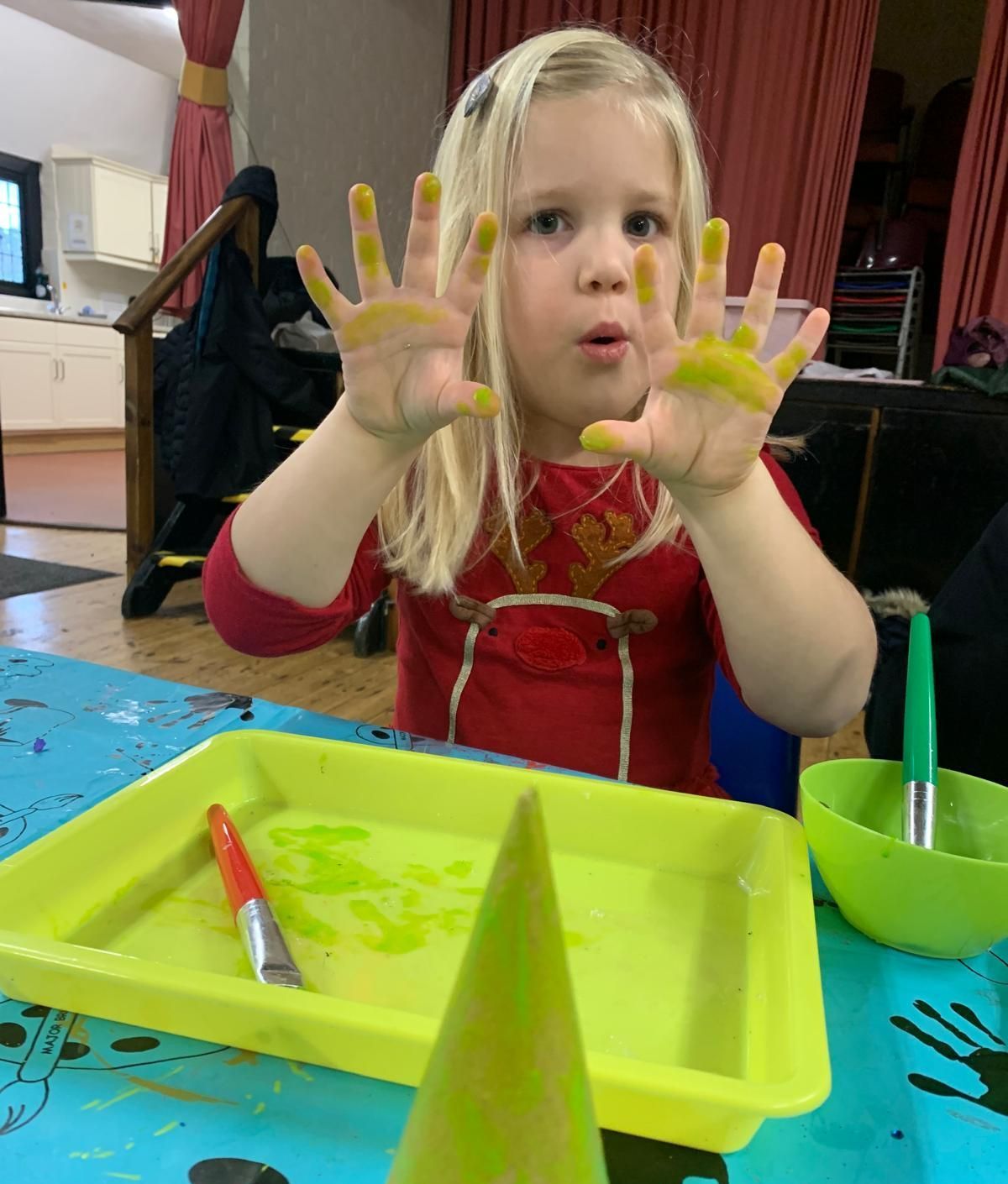 A little girl is sitting at a table with her hands painted yellow at Dragonfly crafts