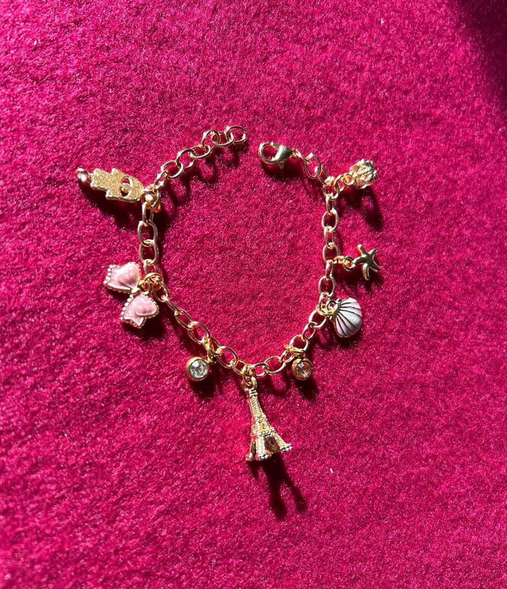 A gold bracelet with pink charms is sitting on a pink surface for charm party  at Dragonfly crafts parties
