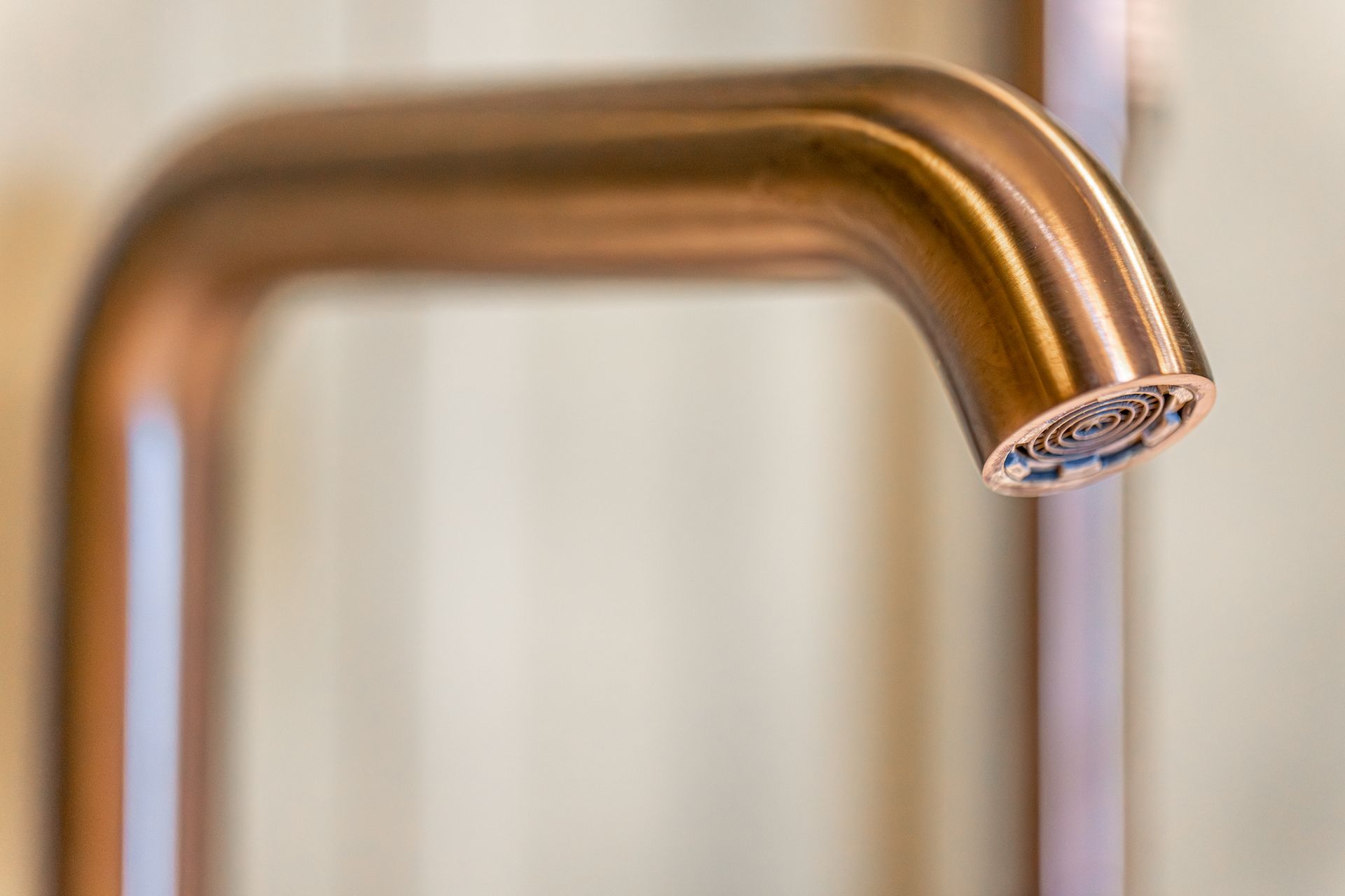 Close-up of a bronze kitchen faucet with a blurred beige background