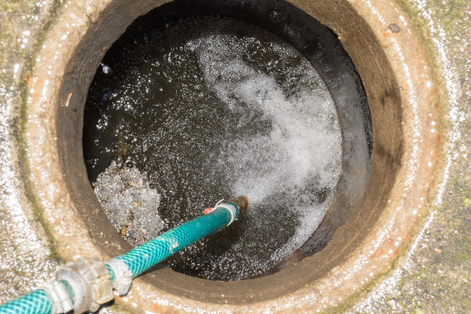Green hose spraying water into a round concrete drain hole
