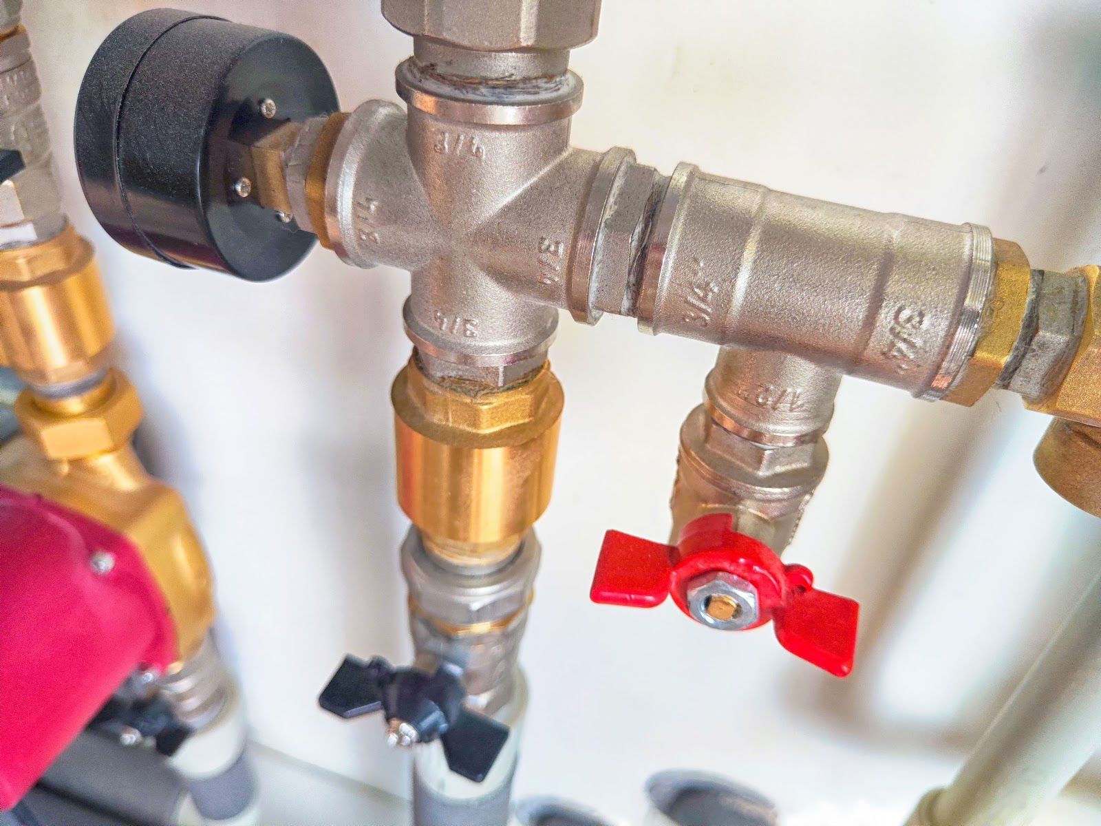 Close-up of plumbing valves and pipes with red and black shutoff handles on a white wall