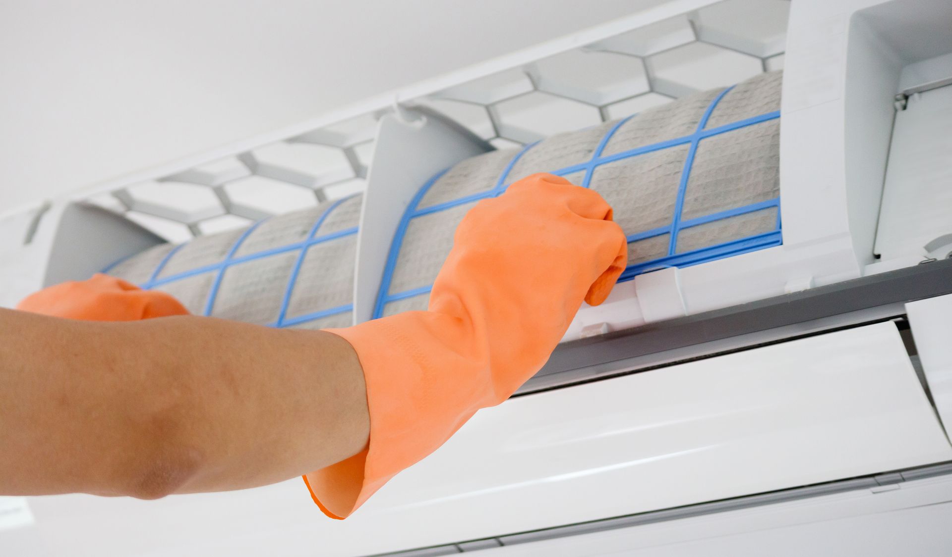A person wearing orange gloves is cleaning an air conditioner.