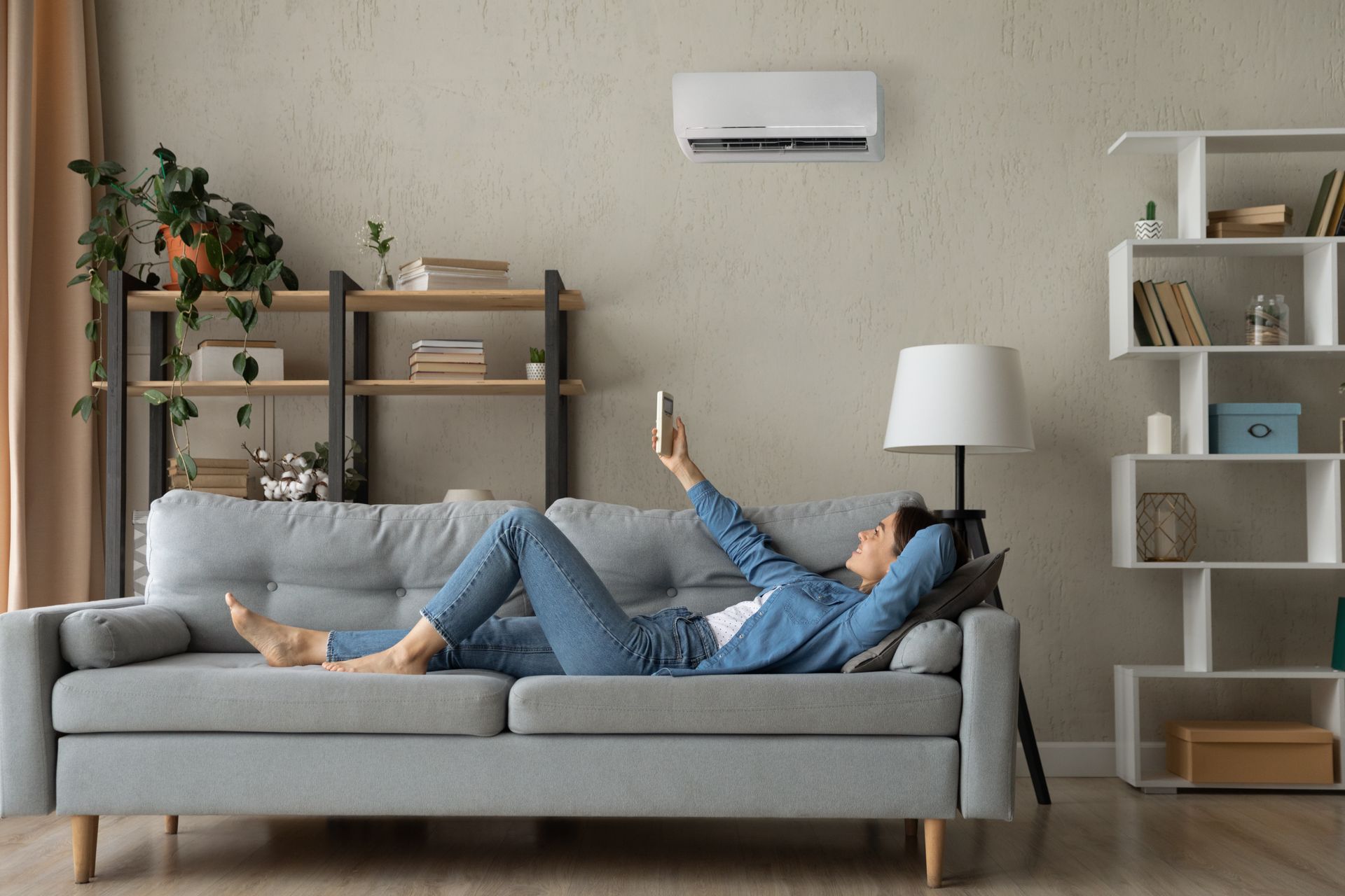 A woman is laying on a couch in a living room using an air conditioner.