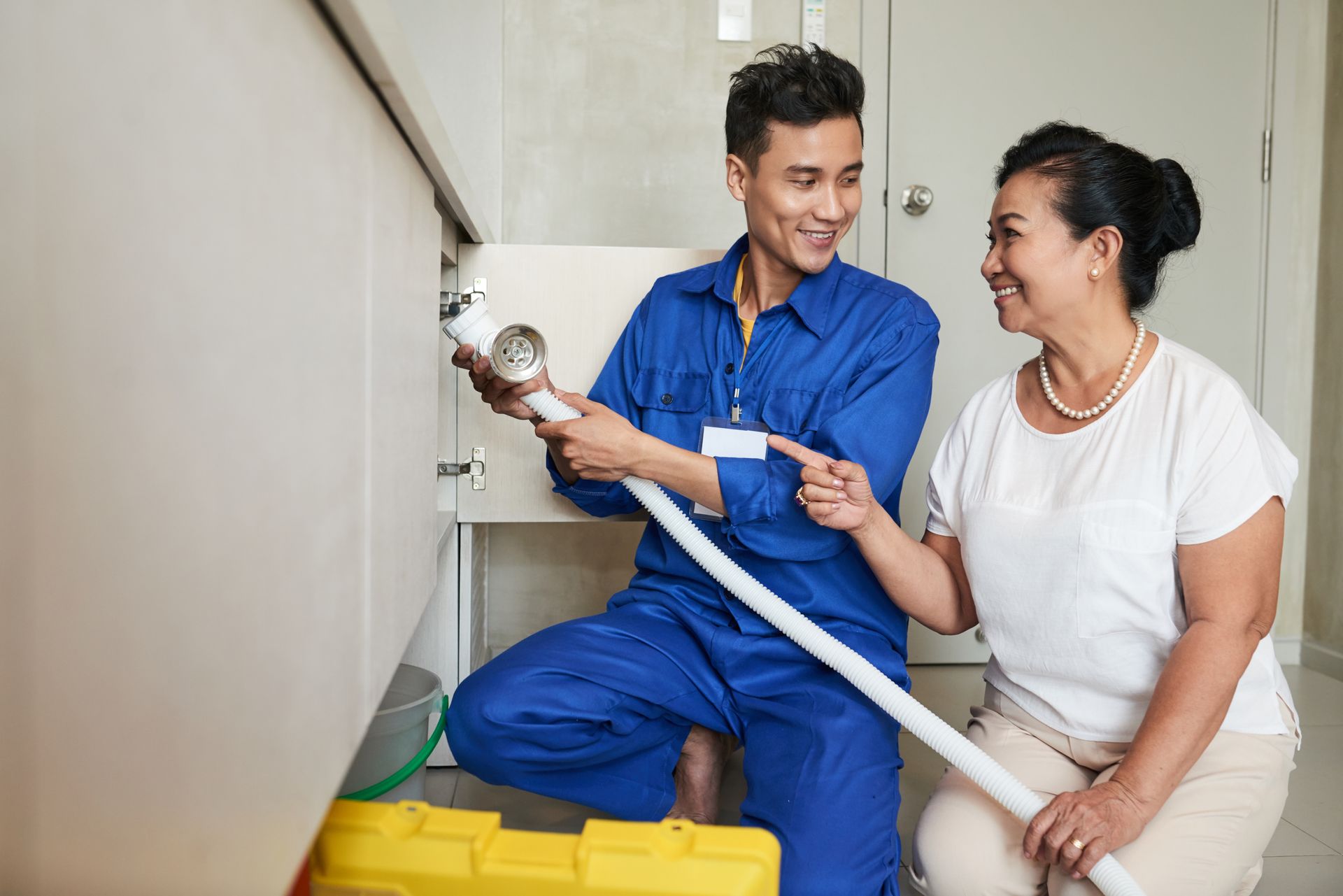 A plumber is fixing a sink with a woman sitting next to him.