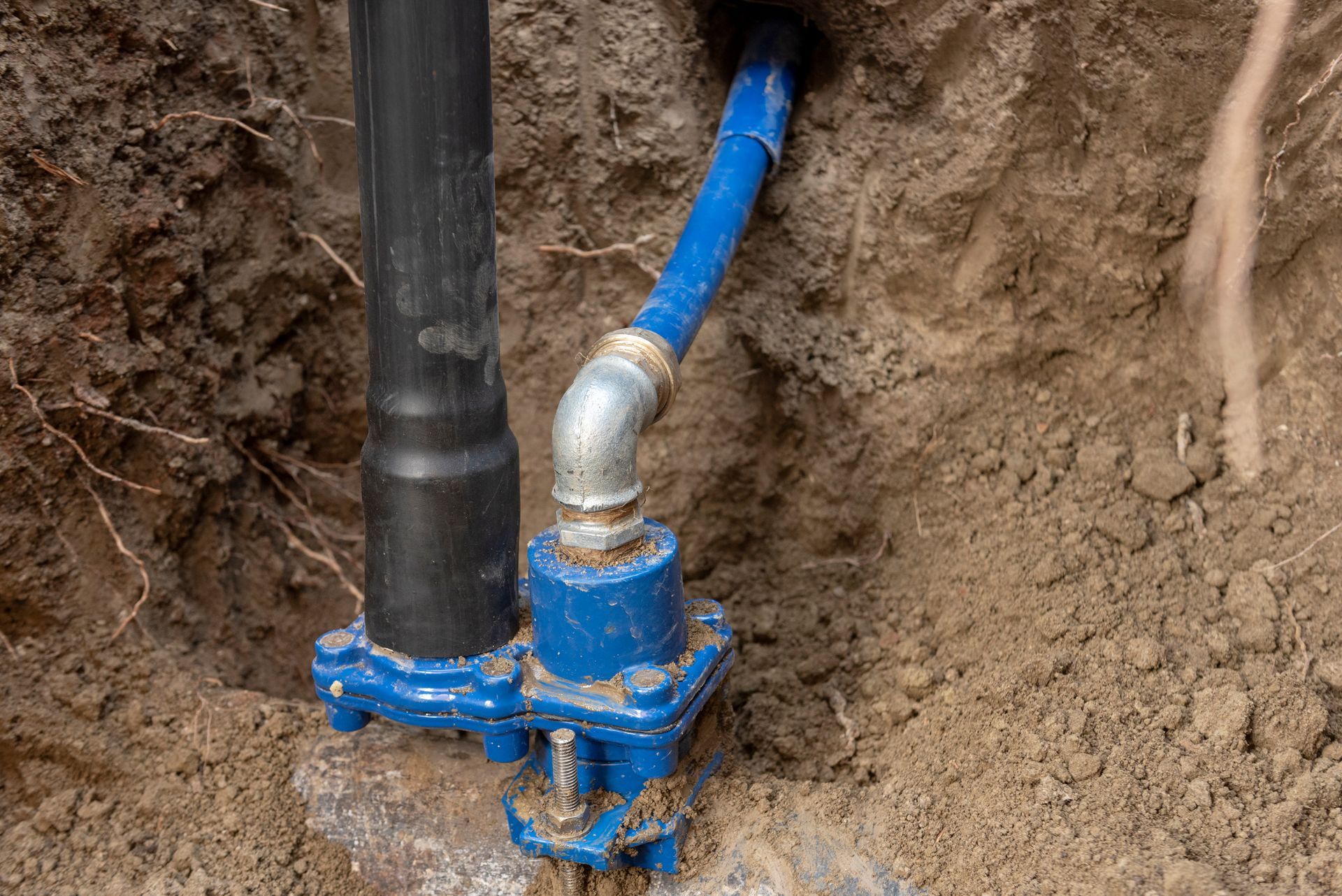A blue pipe is connected to a black pipe in the dirt.