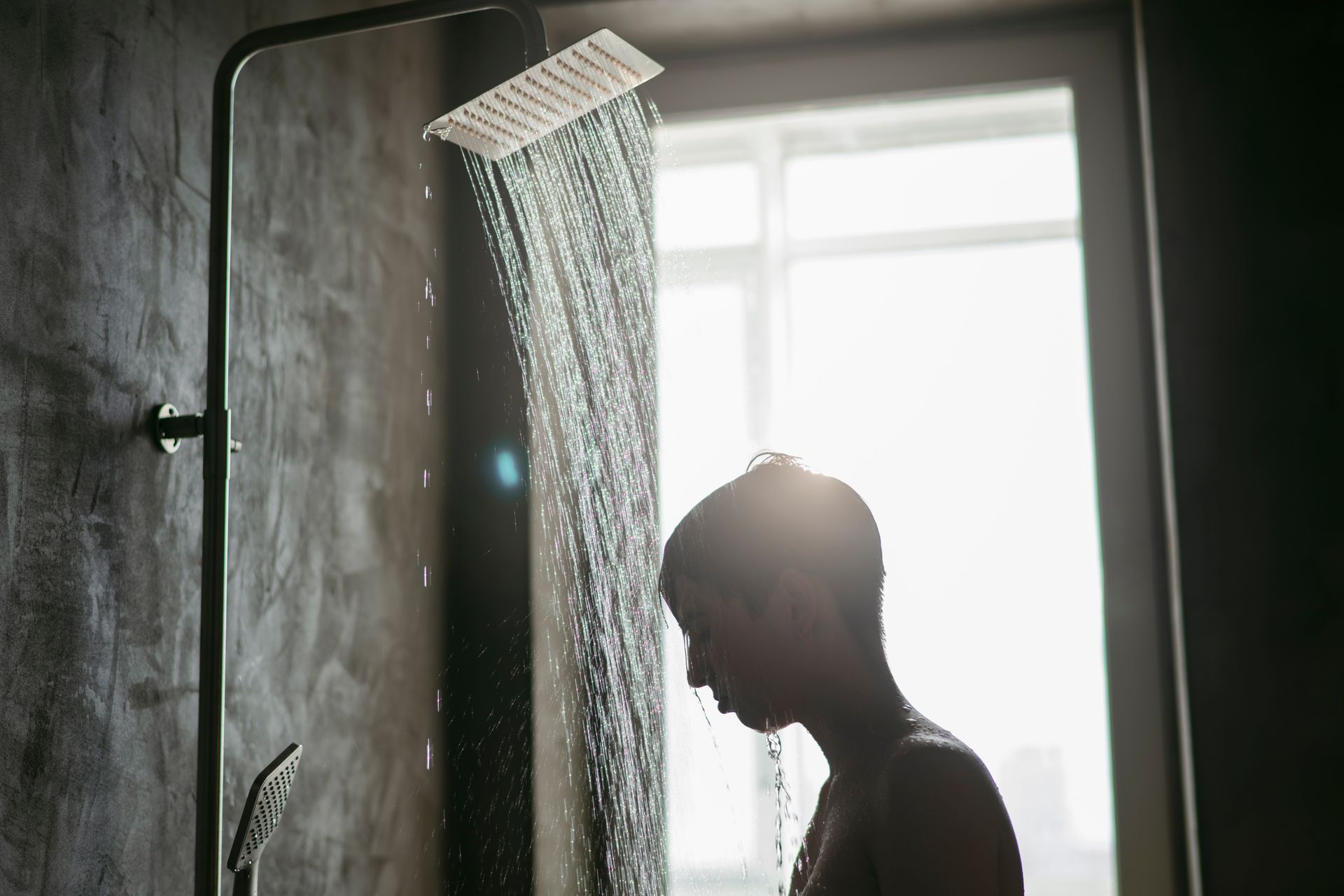 A man is taking a shower in a bathroom next to a window.