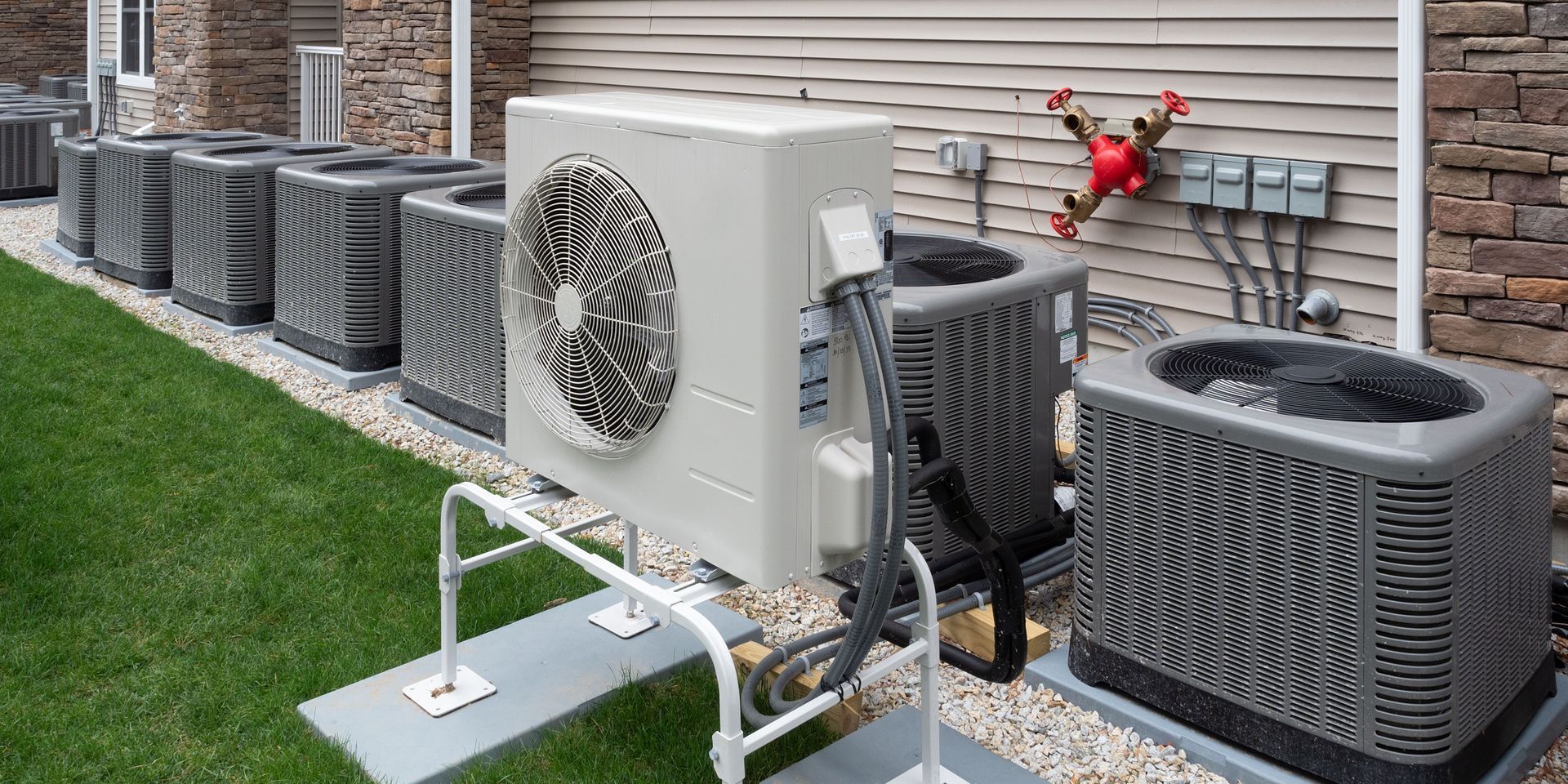 A row of air conditioners are sitting outside of a house.