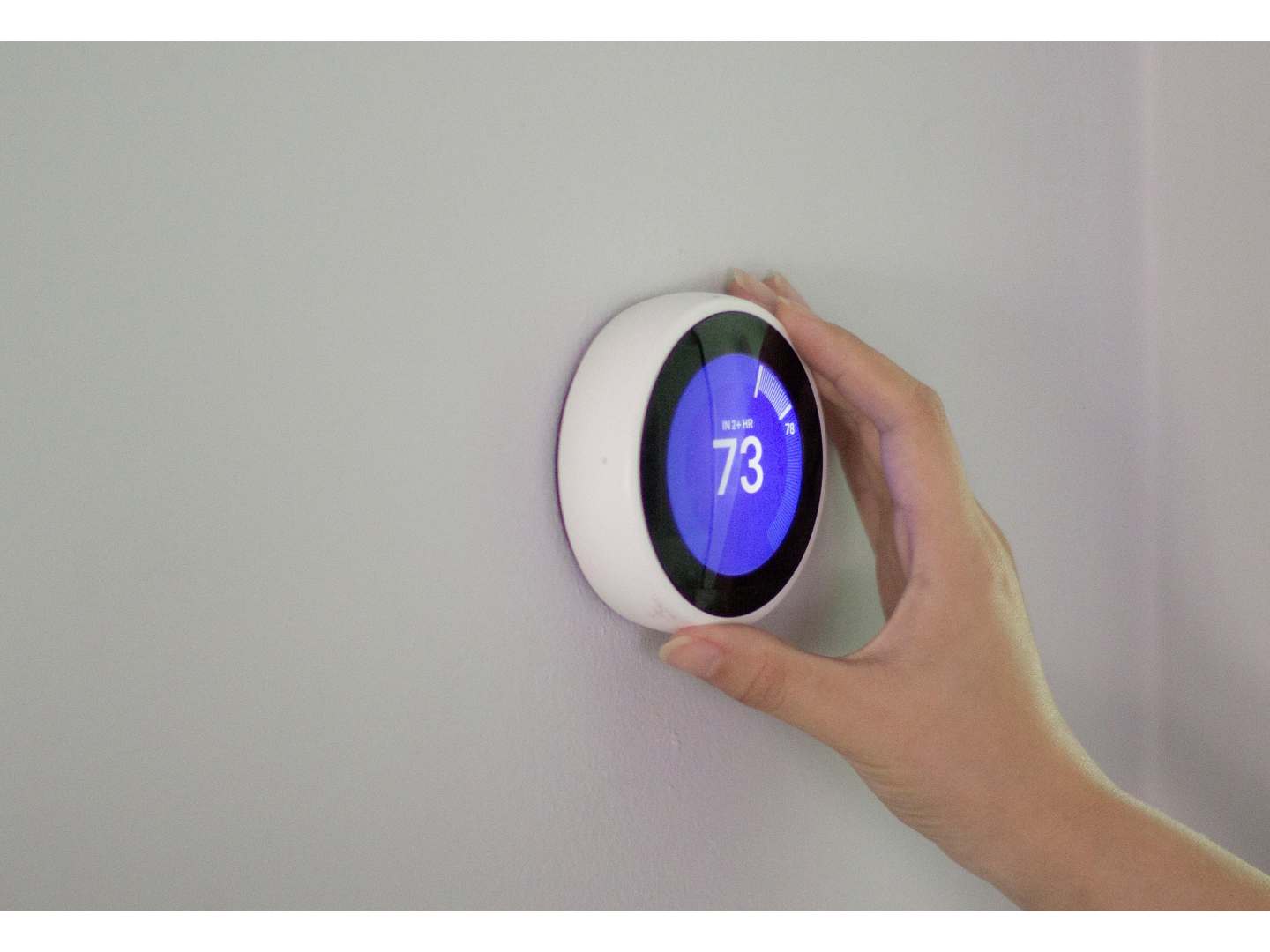 A person is adjusting a thermostat on a wall.