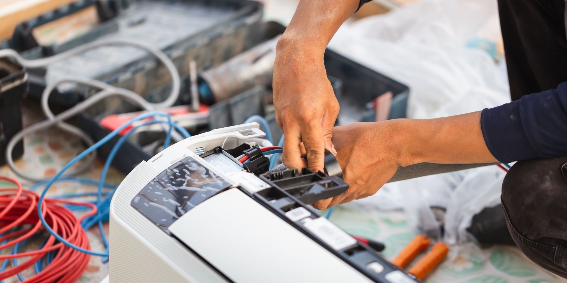 A man is fixing an air conditioner with a pair of pliers.