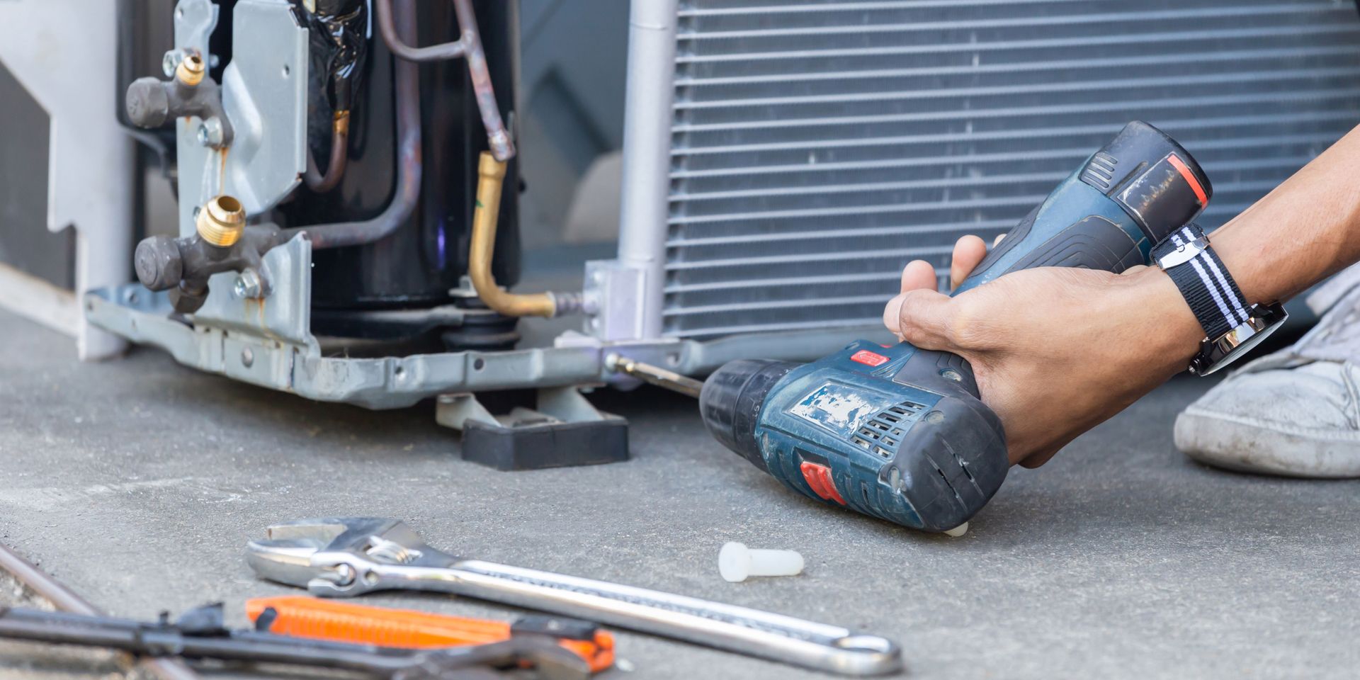 A person is fixing an air conditioner with a drill.