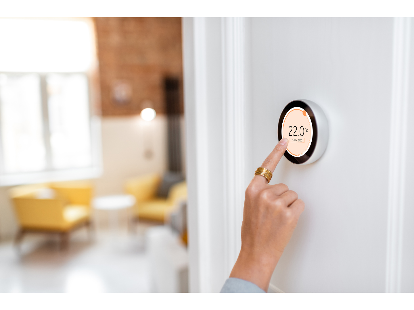 A person is pressing a button on a thermostat in a living room.
