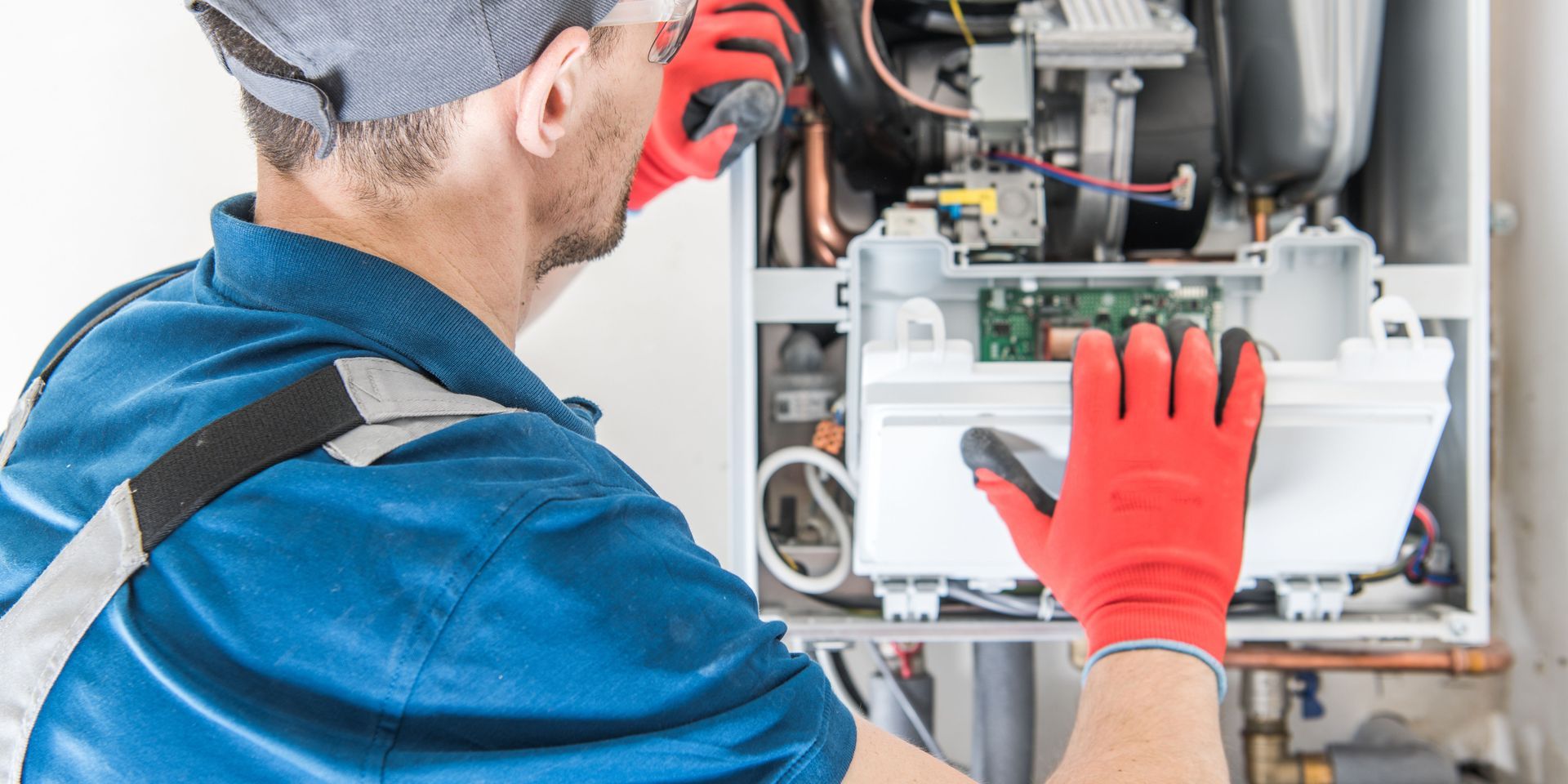 A man wearing red gloves is working on a boiler.