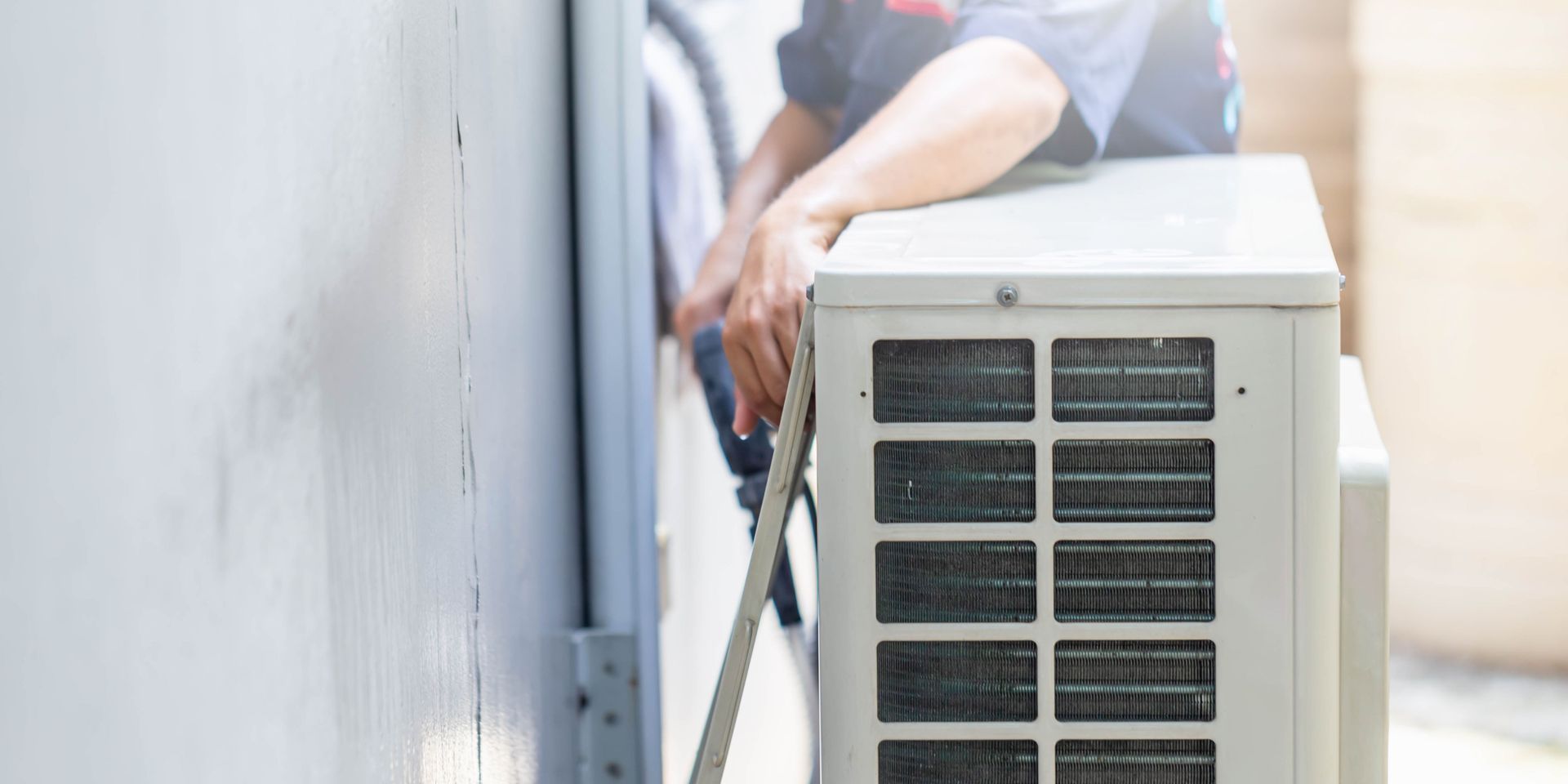 A man is installing an air conditioner on the side of a building.