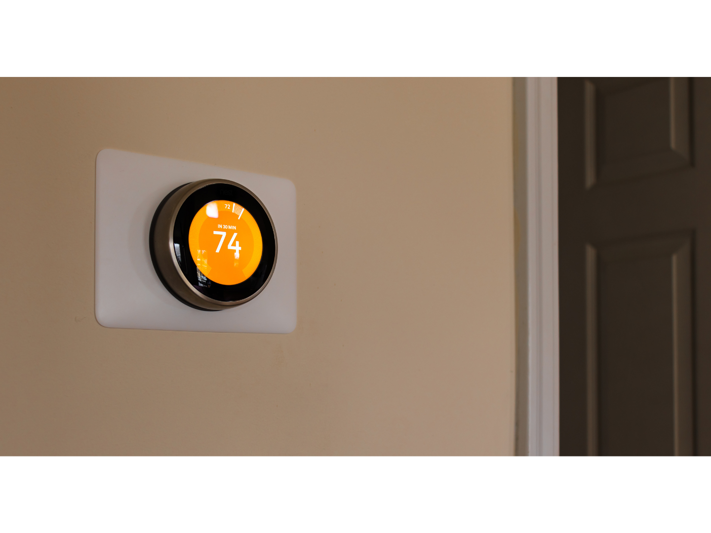 A smart thermostat is mounted on a wall next to a door.
