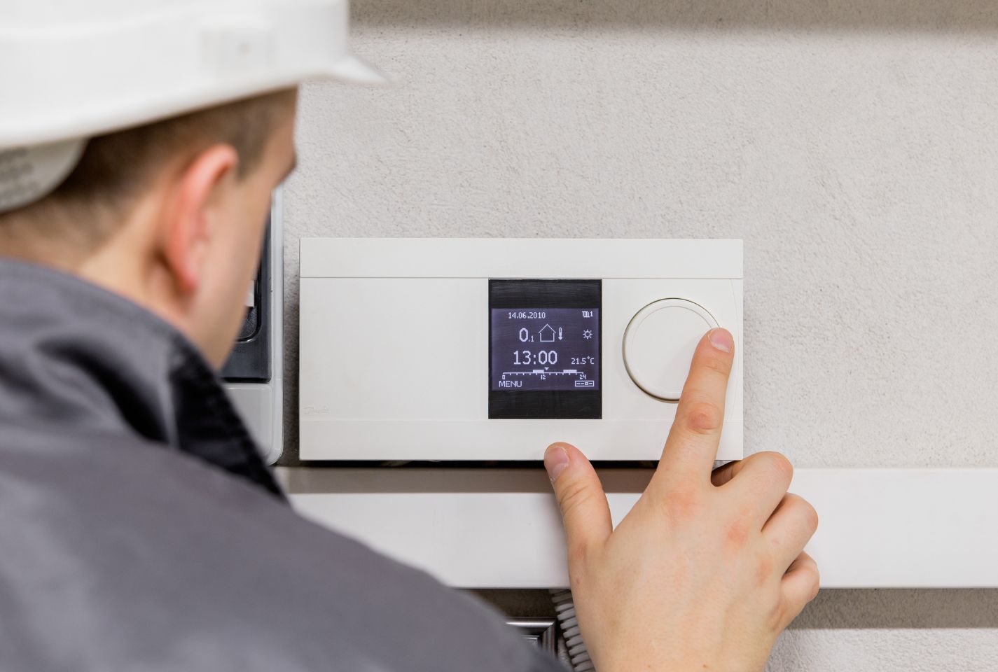 A man is adjusting a thermostat on a wall.
