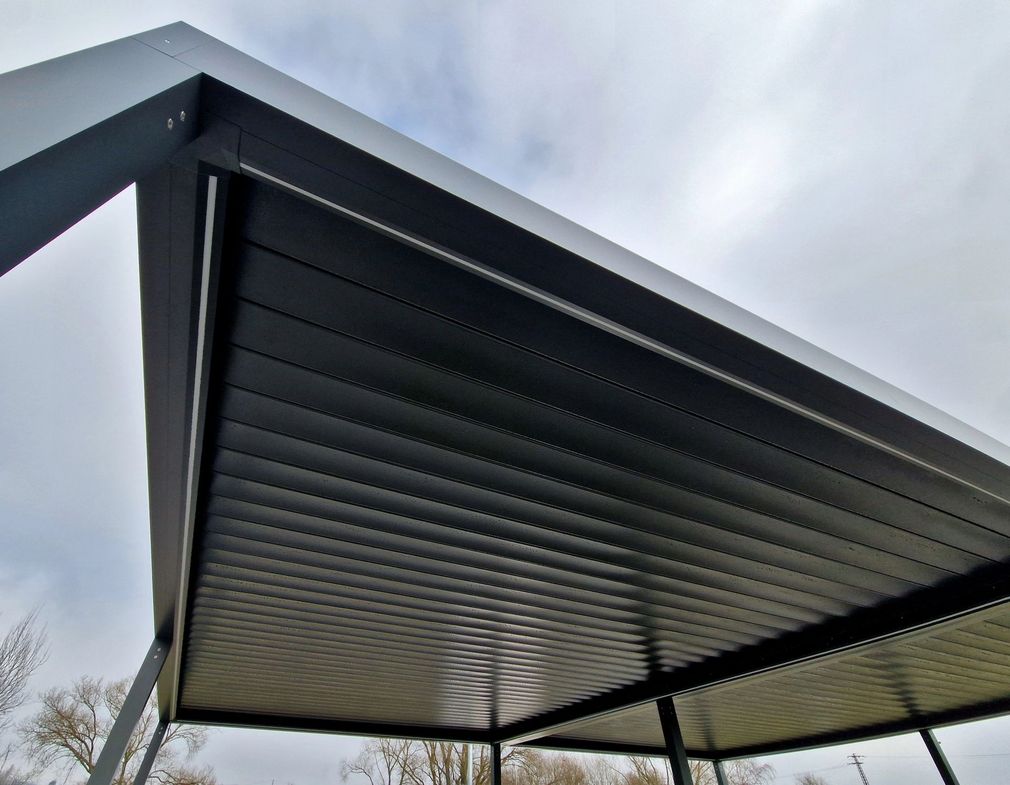 Primo piano di un tetto a pergola nera con lamelle orientabili sullo sfondo di un cielo nuvoloso.