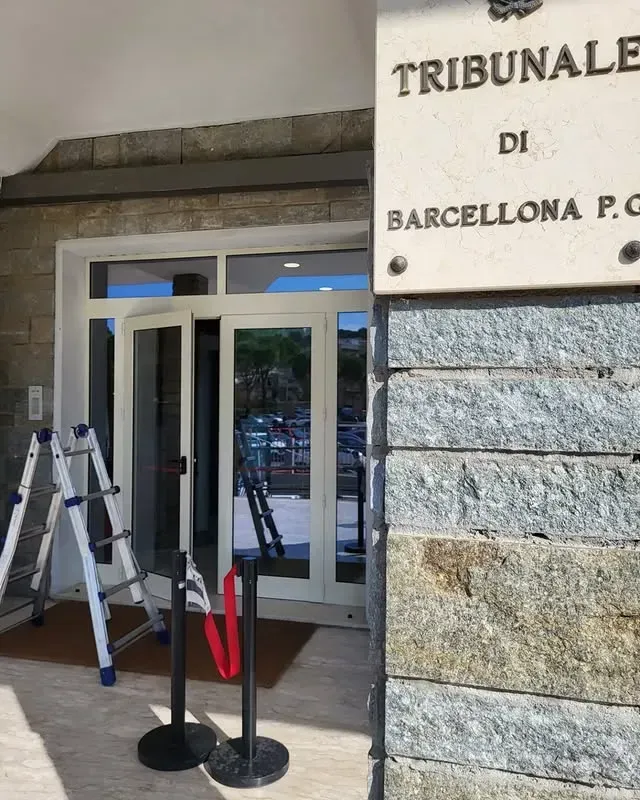 Ingresso di un tribunale con un cartello recante la scritta “TRIBUNALE DI BARCELLONA PG” e paletti all'esterno