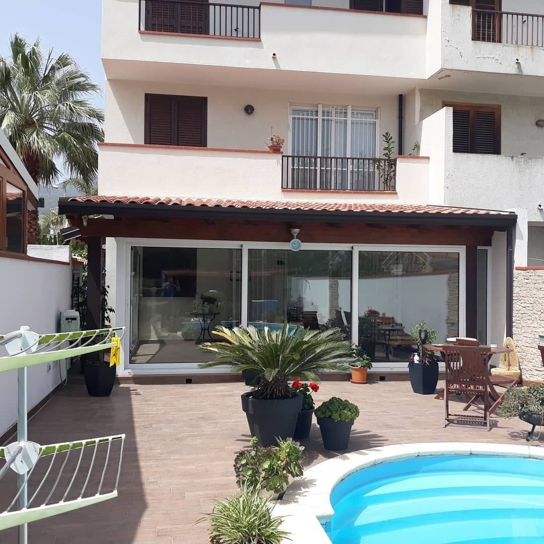 Patio con piscina, piante in vaso e una casa moderna con porte scorrevoli in vetro.