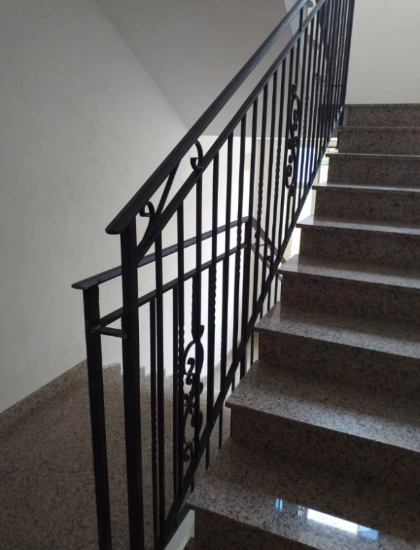 Scala interna con ringhiera in metallo scuro e gradini rivestiti di moquette marrone su pareti bianche.