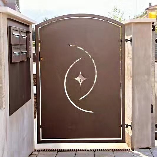 Cancello carrabile in metallo marrone con decorazione a spirale bianca tra pilastri in cemento.