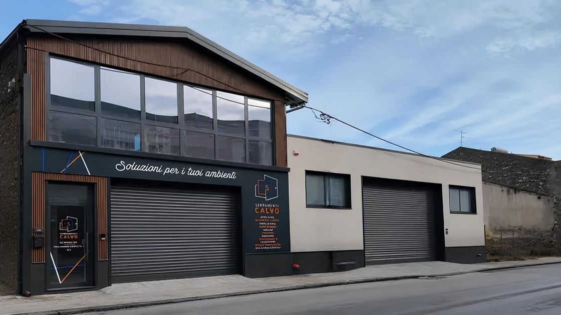 Edificio affacciato sulla strada con facciata in legno scuro e due grandi portoni da garage sotto un cielo azzurro.