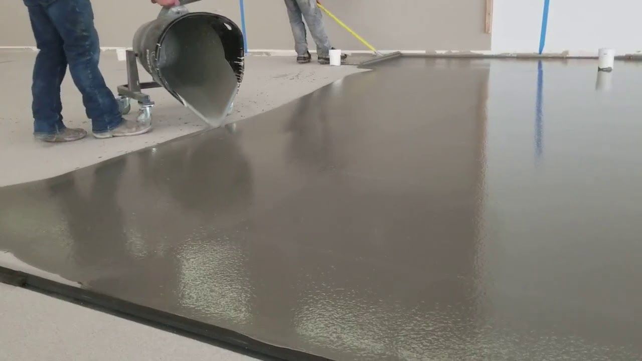 Workers pour gray concrete to level a floor in an indoor construction site.