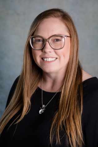 A woman wearing glasses and a necklace is smiling for the camera.