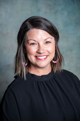 A woman wearing a black shirt and a necklace is smiling for the camera.