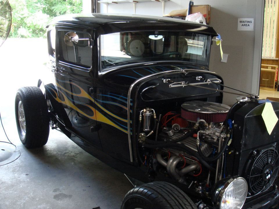 Black vintage hot rod with flames, exposed engine, and chrome grille parked in a garage