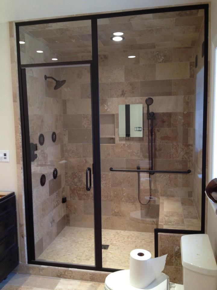 Glass-walled beige tiled shower with black trim and grab bars in a bathroom