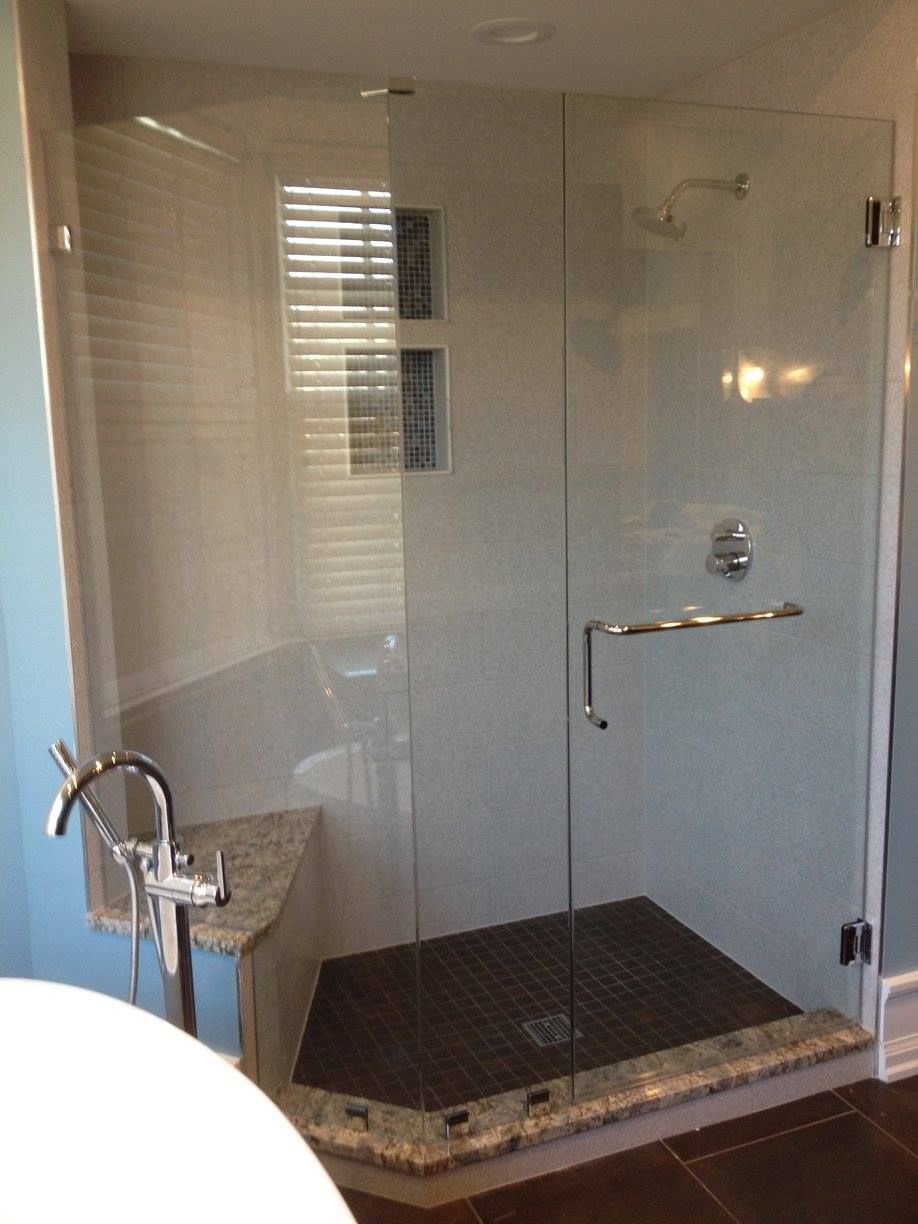 Glass walk-in shower with chrome fixtures and pebble-textured floor in a tiled bathroom