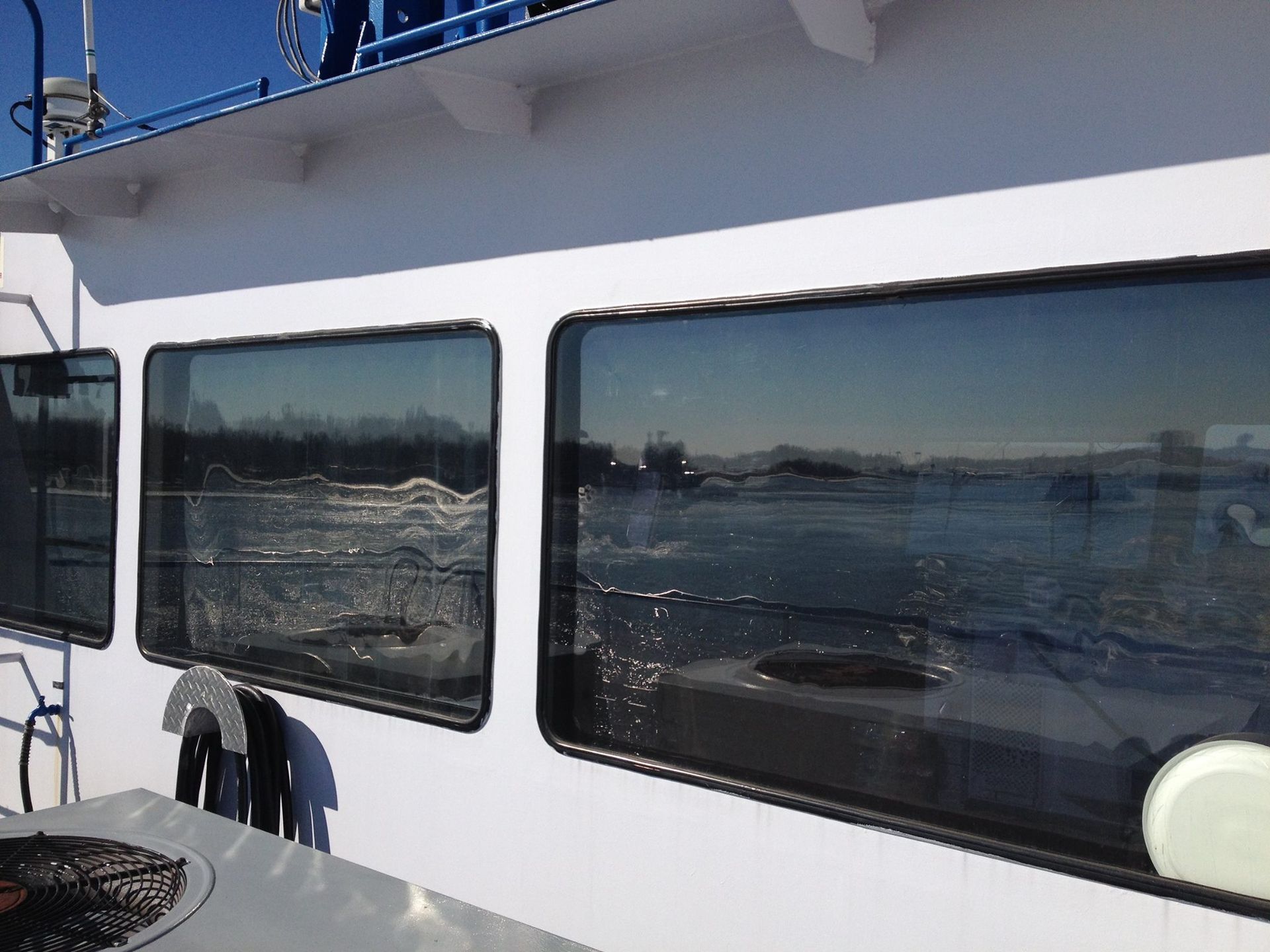 White boat cabin with dark windows reflecting sparkling water under a bright sky