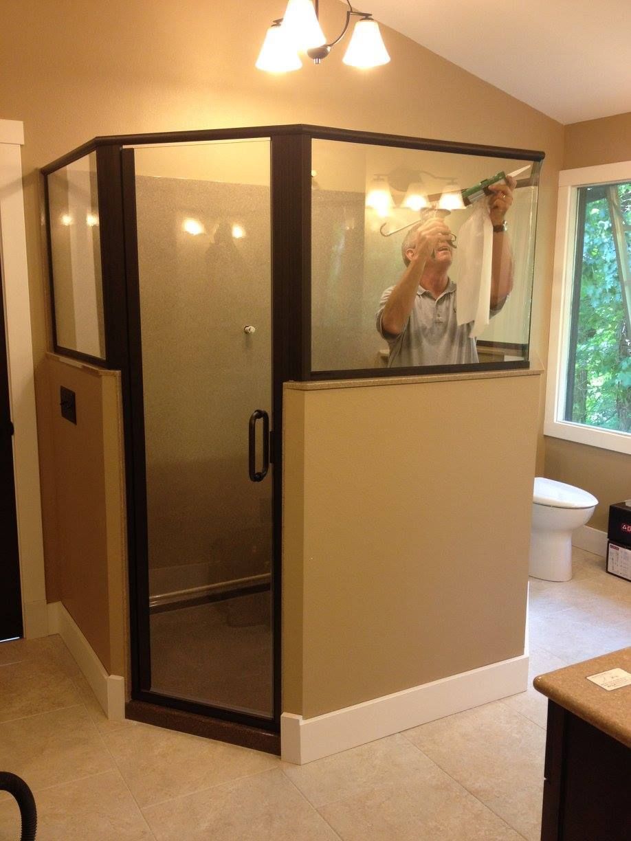 Glass-walled shower enclosure in a beige bathroom, with a person visible inside.
