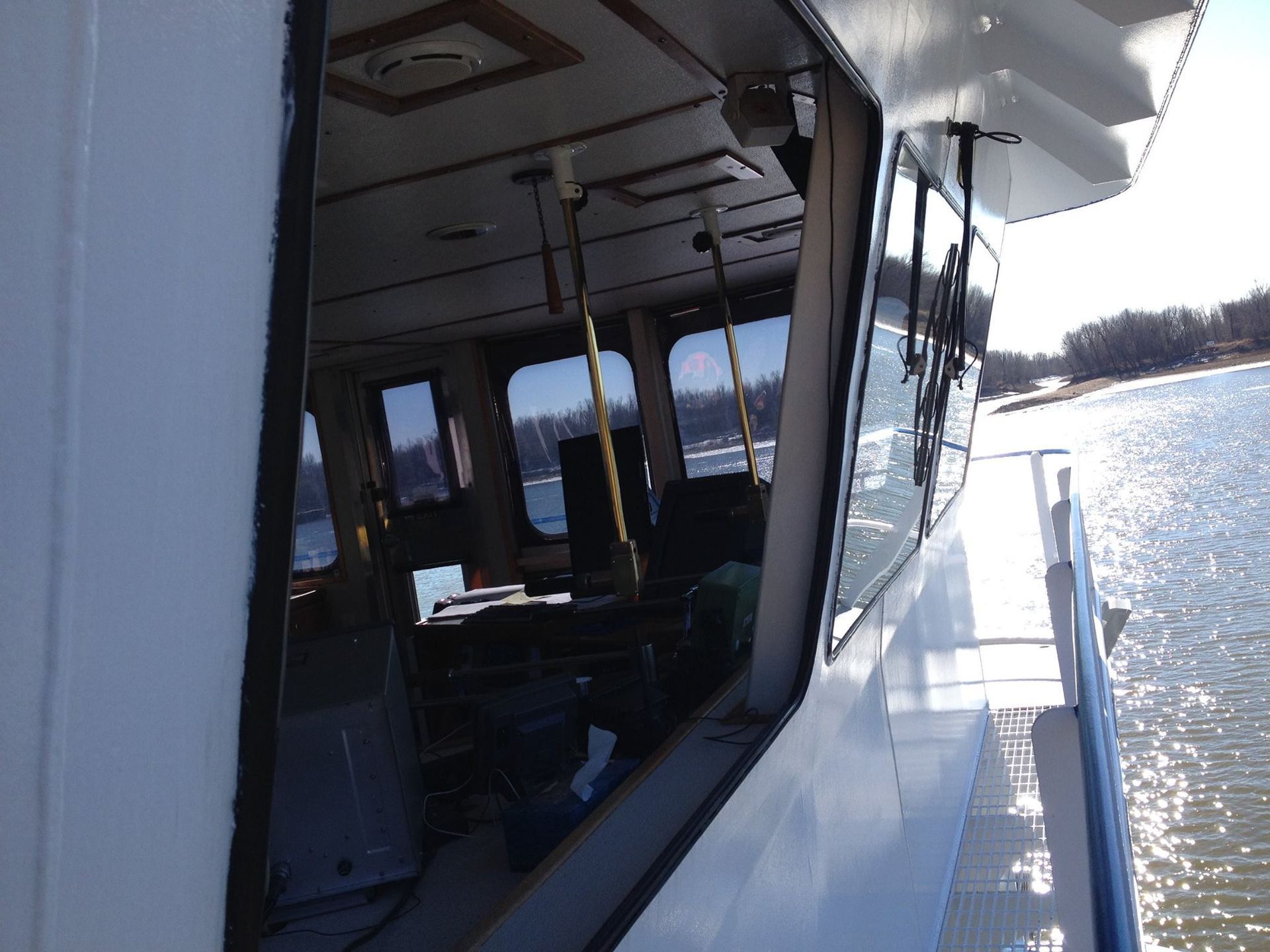 Boat deck beside sunlit water with windows reflecting the shoreline