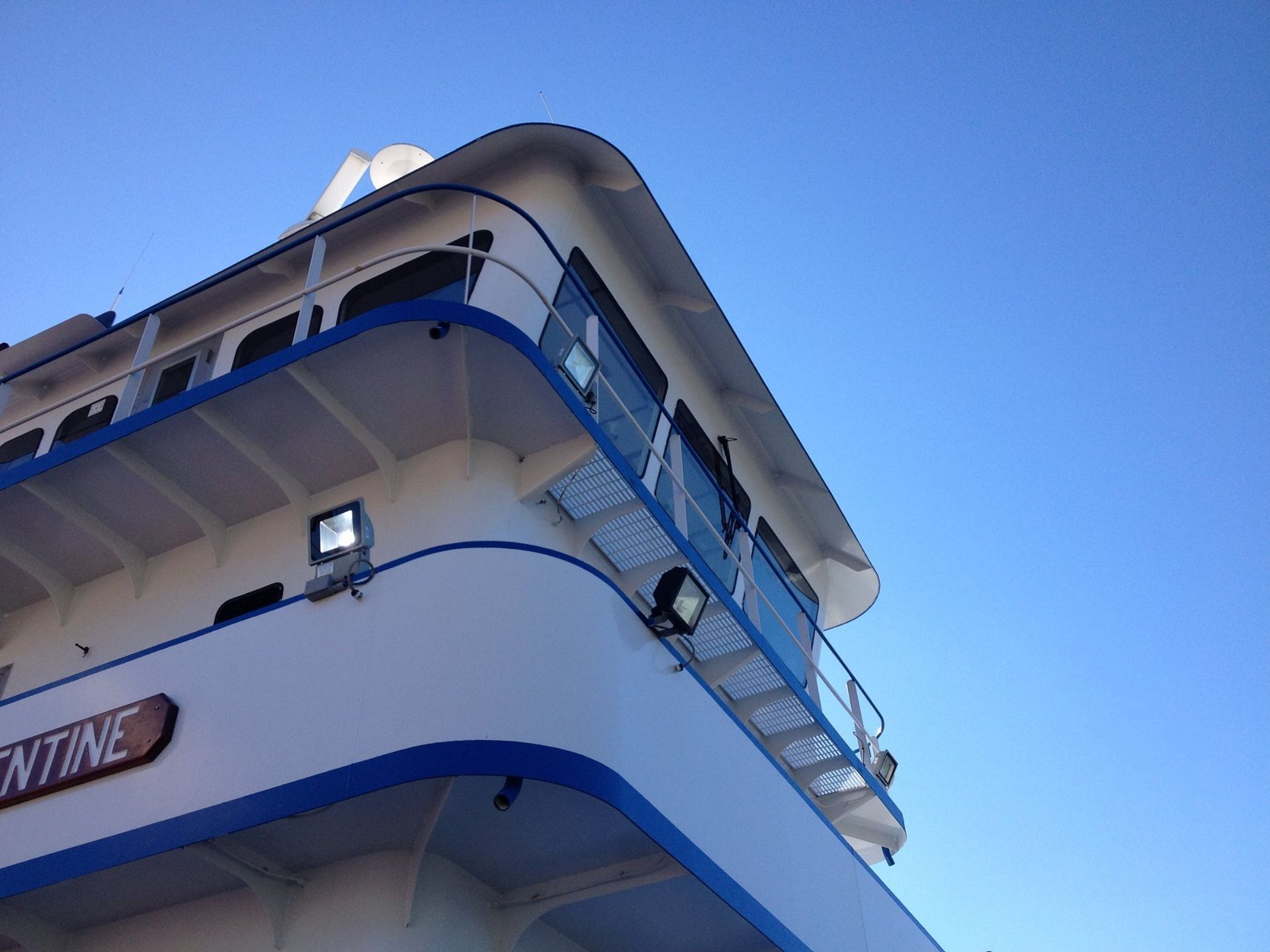 White and blue ship bow against a clear blue sky, with railings and windows visible