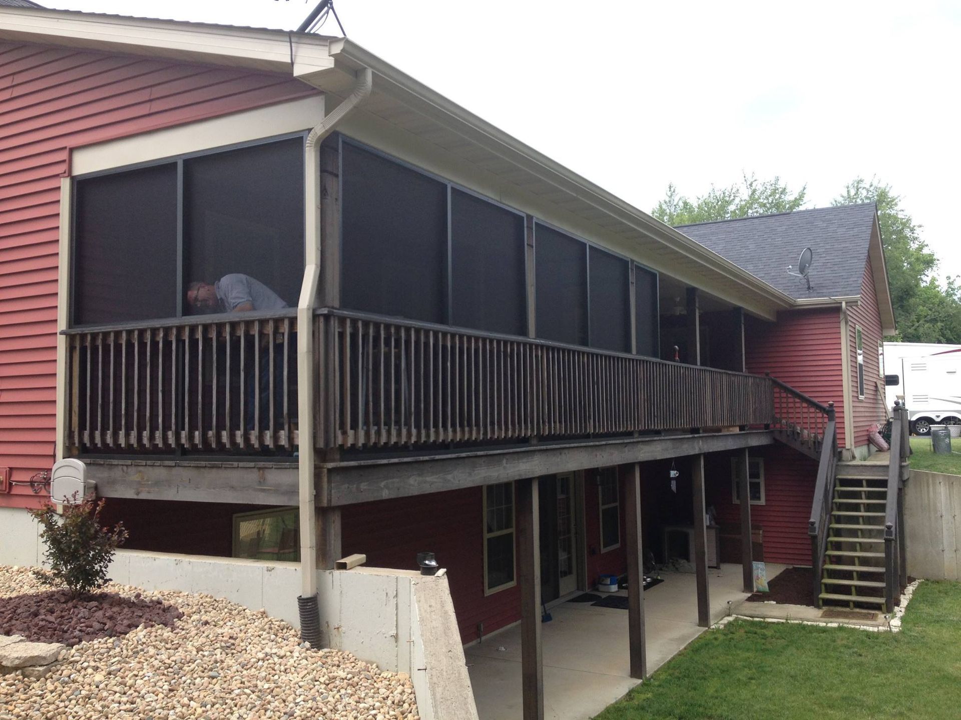 Screened porch on a red house with wooden railing and stairs to a lower level