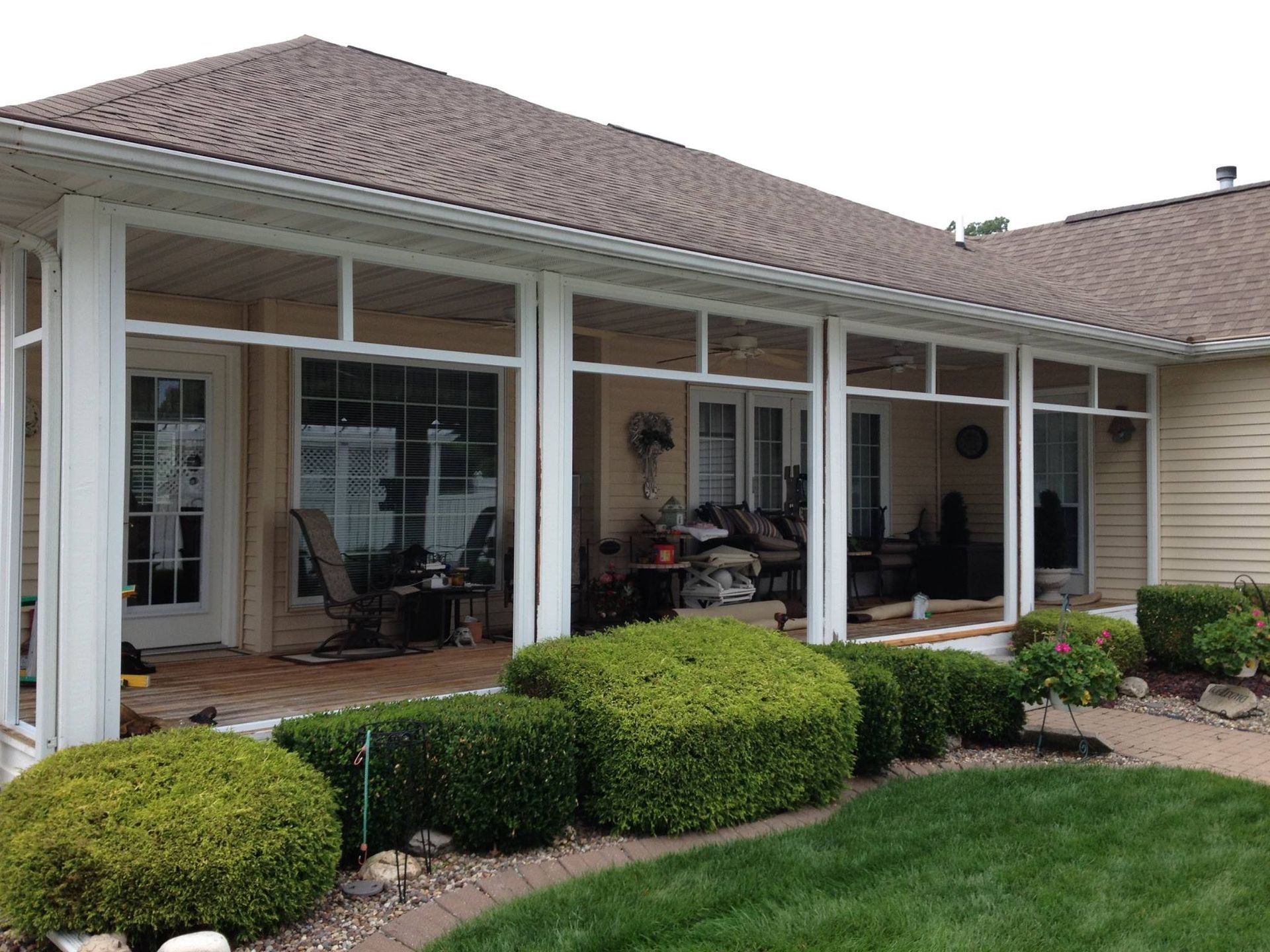 Back patio with white columns, brick flooring, hedges, and lawn beside a single-story house