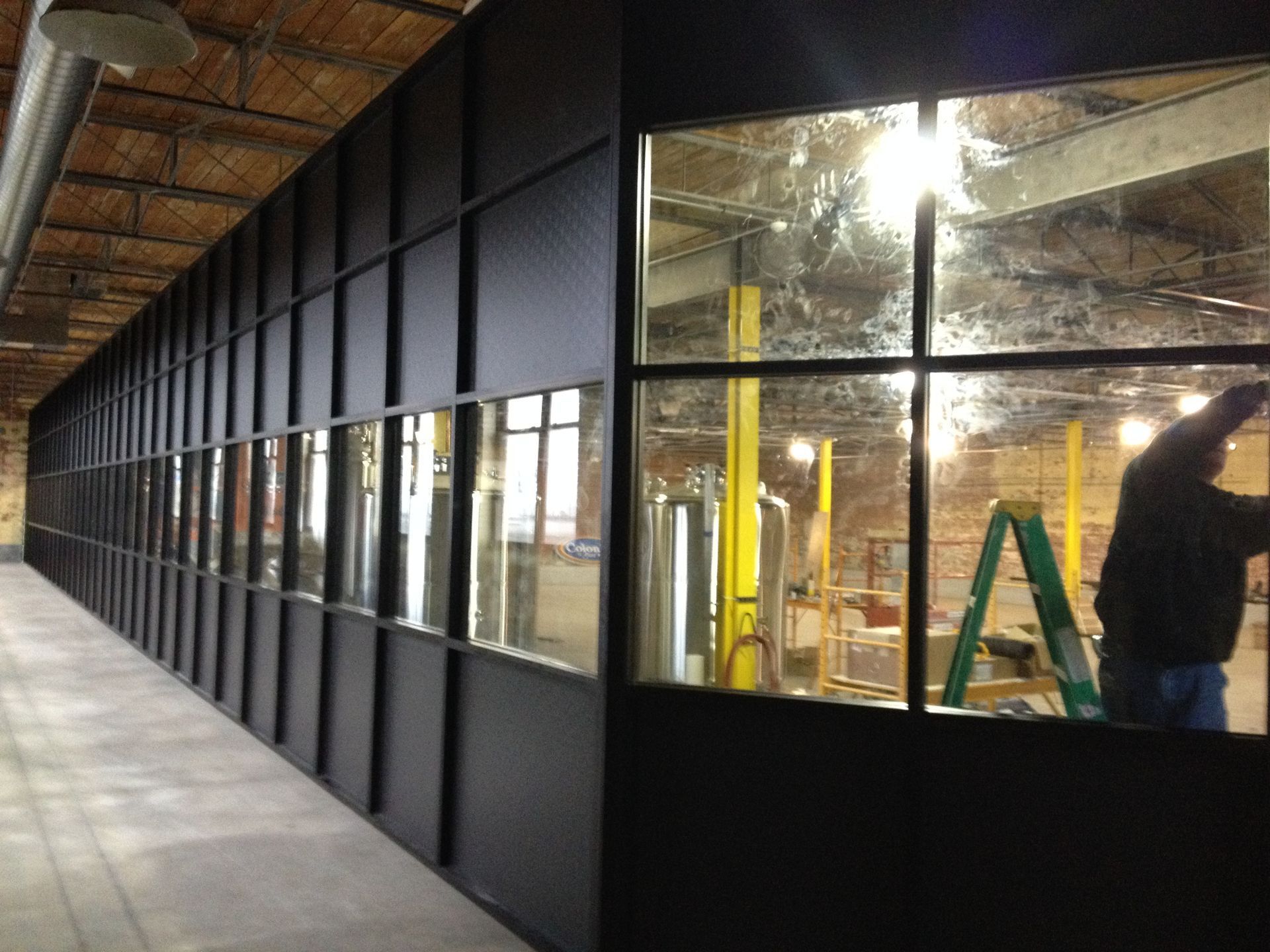 Industrial hallway with black wall panels and windows into a lit workspace under construction